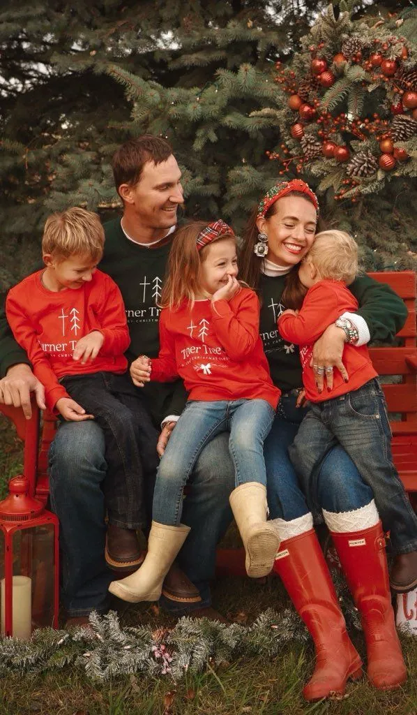 The Turner family on a red bench in front of the Christmas trees
